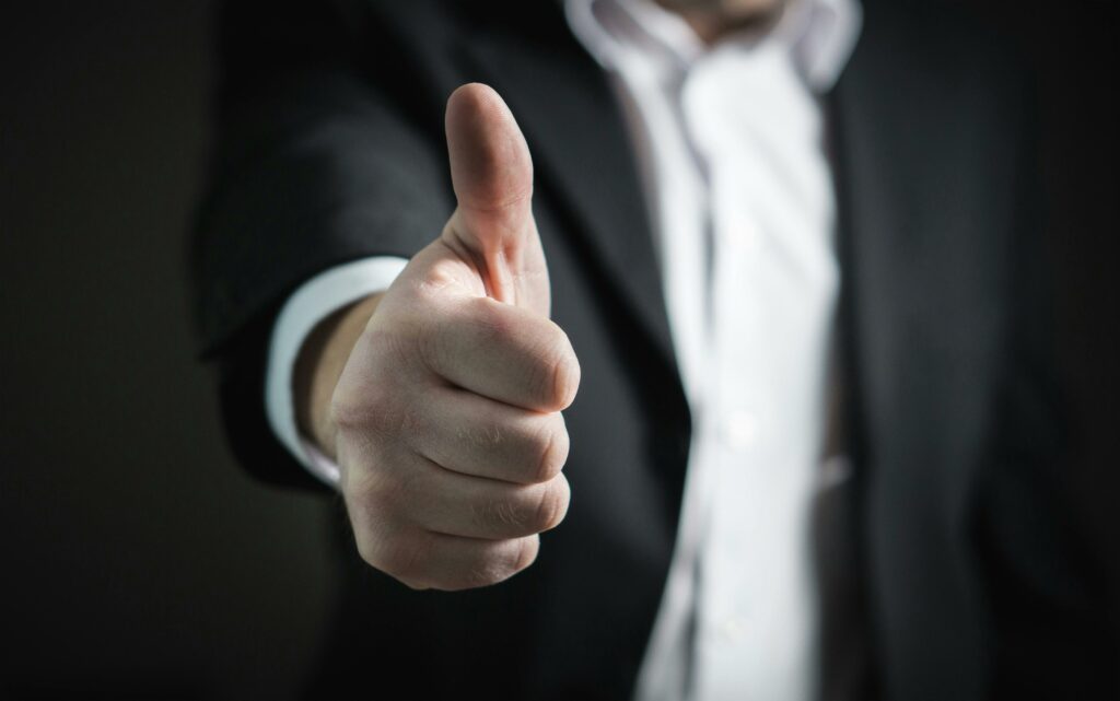 A man in a suit gives. a thumbs up to the camera because of his positive brand reputation for his corporation.